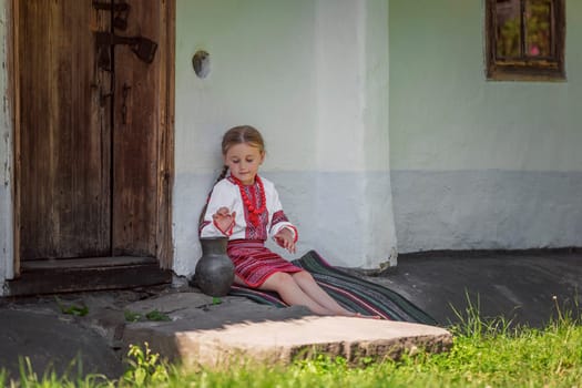 A lovely girl dressed in her colorful traditional clothing is sitting by a charming door on a bright sunny day
