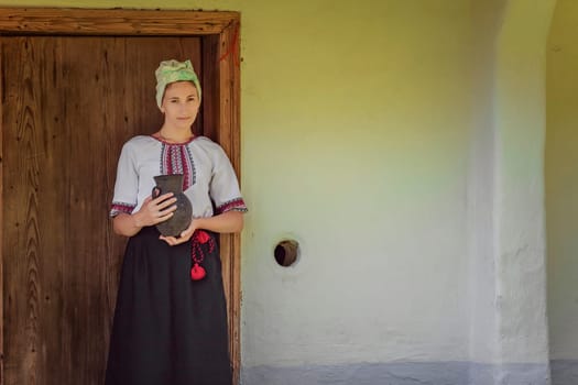 A woman dressed in beautiful traditional attire poses proudly with a decorative pot by an old wooden door