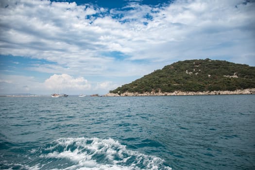 Boat near an island in the Mediterranean Sea, a wave on blue water and white foam on the tops of the waves from under the side of a sailing boat,