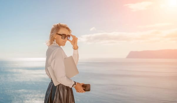 Business woman on nature in white shirt and black skirt. She works with an iPad in the open air with a beautiful view of the sea. The concept of remote work