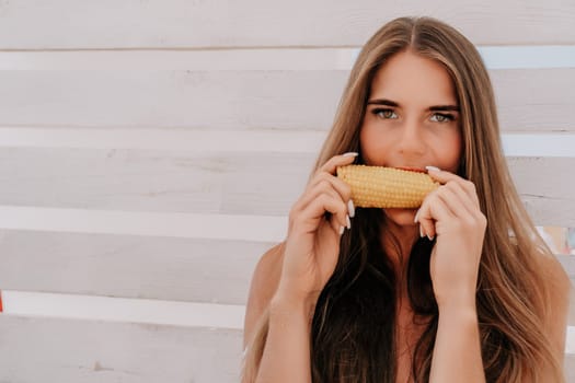 Healthy vegetarian hipster woman in summer outfit eat grilled corn and look to camera. Sexy lady on sea beach sunset or ocean sunrise. Travel, explore, active yoga and meditation lifestyle concept.