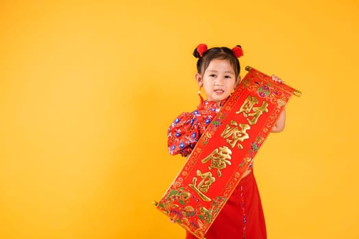 Chinese New Year. Happy Asian Chinese little child girl smile wearing red cheongsam qipao Spring festival couplets (Character FU means fortune, blessing), studio short isolated on yellow background