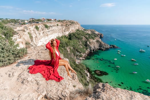 Woman red dress sea. Happy woman in a red dress and white bikini sitting on a rocky outcrop, gazing out at the sea with boats and yachts in the background