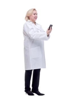 Cheerful young woman doctor standing and using smartphone over white background