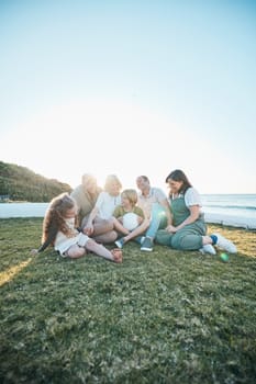 Family, grandparents and kids on grass by ocean for bonding, relationship and relax together. Nature, parents and happy grandmother, grandfather and children on holiday, vacation and travel by sea.