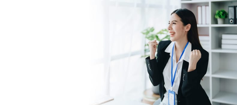 Portrait of a woman business owner showing a happy smiling face as he has successfully invested her business using computers and financial budget documents at work.