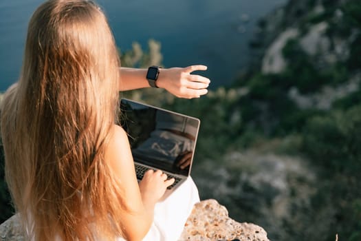 Freelance women sea working on the computer. Good looking middle aged woman typing on a laptop keyboard outdoors with a beautiful sea view. The concept of remote work