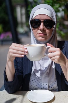 Caucasian woman in hijab drinking coffee in outdoor cafe