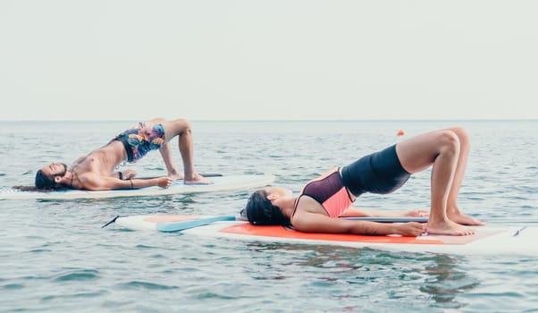 Woman man sup yoga. Happy young sporty couple practising yoga pilates on paddle sup surfboard. Female stretching doing workout on sea water. Modern family outdoor summer sport activity