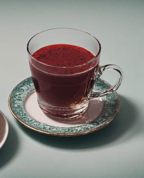 A cup of red liquid sits on a green plate. The cup is half full and the liquid is a deep red color. The plate is decorated with a floral pattern