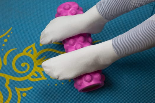 Female feet rolling workout roller on yoga mat during sports exercise for muscle strengthening and stretching at home. Sports equipment cylindrical roll for sports at home. Fitness girl takes care of legs health