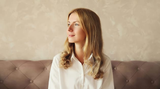 Happy satisfied young woman thinks looking out the window in early morning sitting on couch in the living room at home