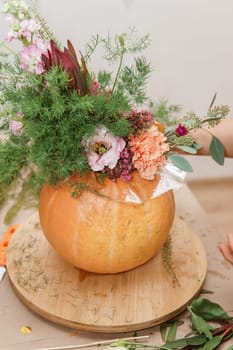 Flower arrangement in a pumpkin, autumn interior decor. Creating handmade autumn decor