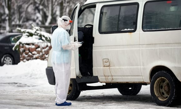People in protective suits helping a sick person outdoors, coronavirus concept. Ambulance car.
