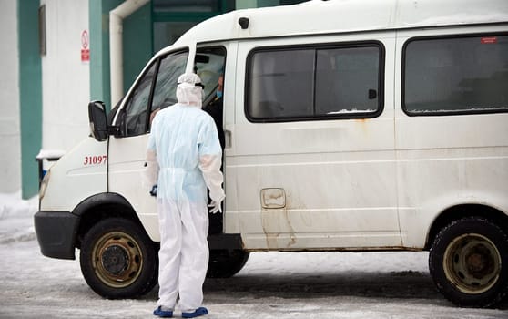 People in protective suits helping a sick person outdoors, coronavirus concept. Ambulance car.