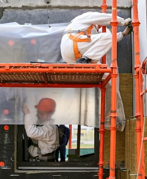 A builder measures the area wearing helmets, goggles and protective equipment at a construction site indoors. Installation of apartment insulation.