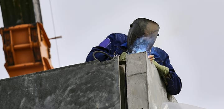 a welder welds concrete slabs during an outdoor construction project on an apartment building.