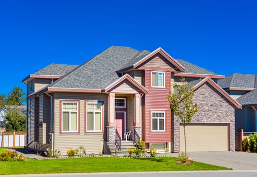New family house on sunny day with landscaped lawn in front and blue sky background. New house with concrete driveway and asphalt road in front.