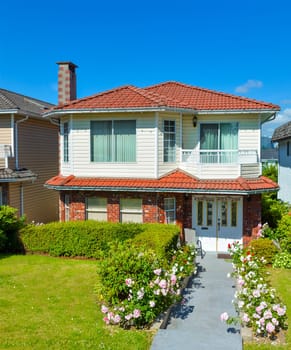 A perfect neighborhood. Average family house with concrete pathway to the entrance. Family residence on blue sky background