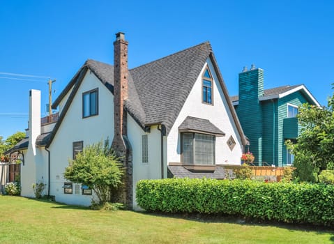 Old style family house with green lawn and hedgerow in front on blue sky background