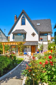 Old style family house with blossoming flowers on front yard and concrete pathway to the entrance