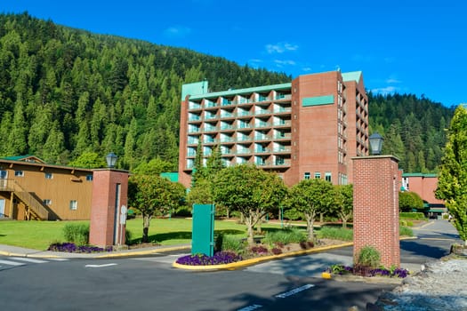 Sand shore of the lake leading to resort building on green mountain and blue sky background