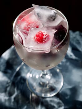 Glass with ice cubes with frozen berries and fruits close-up for a refreshing drink and preservation of seasonal vitamins raspberries, strawberries, cherries, blueberries, mulberries, blackberries
