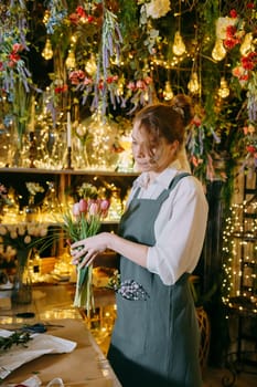 A woman in her florist shop collects bouquets of flowers. The concept of a small business. Bouquets of tulips for the holiday on March 8