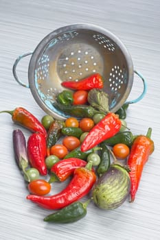 A concept photo of assorted vegetables of peppers, eggplant, and cherry tomatoes by a colander.