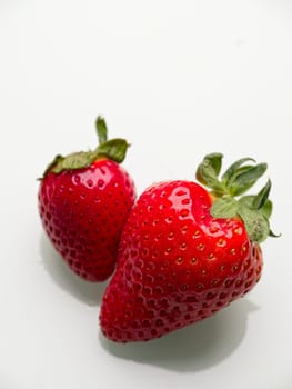 A close up photo of two ripe straberries against a white background.