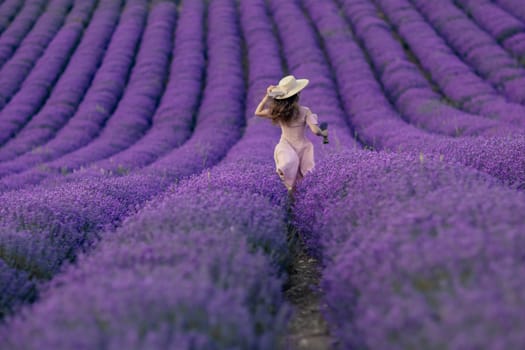 A woman is walking through a field of purple flowers. The field is vast and the flowers are in full bloom. The woman is wearing a hat and a pink dress