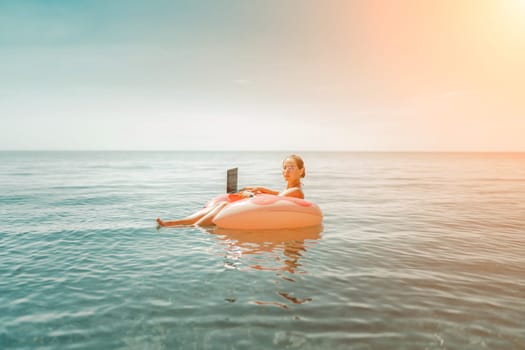 Woman laptop sea. Freelancer woman in sunglases floating on an inflatable big pink donut with a laptop in the sea. People summer vacation rest lifestyle concept