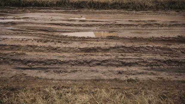 Mud and puddles on the dirt road with sand hills in the background.