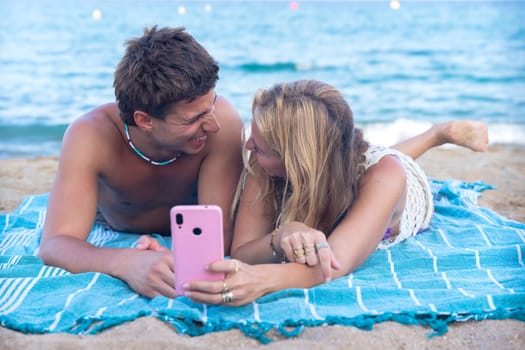 Man and woman hands typing on phone browsing social media phone sitting on beach