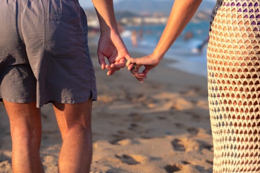 Happy couple in love holding hands and looking at each other on the seashore. A man and a woman are standing on the sand near the ocean. Vows and promises on the seashore.