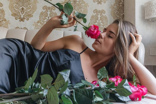 A woman is laying on a bed with a bouquet of red roses in her lap. Concept of romance and intimacy, as the woman is surrounded by the flowers and he is in a relaxed and comfortable position