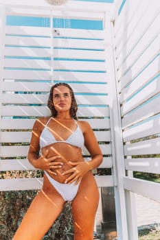 A woman in a bikini stands in front of a white shower stall. She is smiling and she is enjoying the moment.
