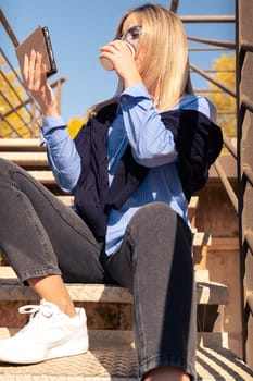 Portrait of a smiling young woman wearing headphones and sunglasses, using a social media app outdoors