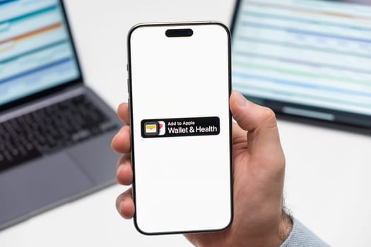 PRAGUE, CZECHIA - JULY, 2024: Wallet and Health logo on the screen of smartphone in mans hand and laptop on the background
