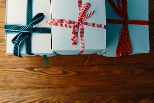 Stack of gift wrapped Christmas presents. A stack of boxes of white colors tied with different ribbons on a wooden background. Flat lay.