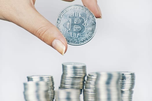 Woman holds Bitcoin coin. Silver bit-coin over many international money coins.