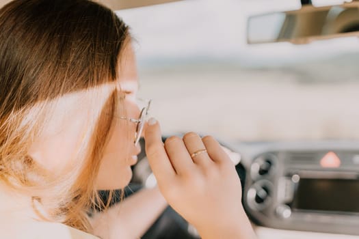 A woman with long blonde hair wears glasses while driving, the sunlight shines through her hair.