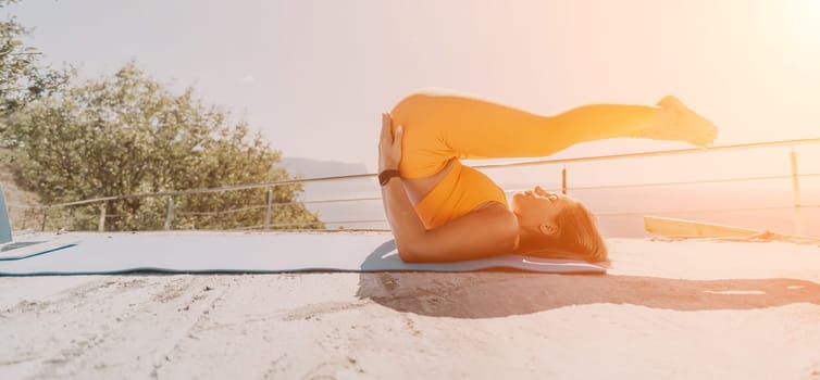 A woman in a yellow sports bra and leggings practices yoga on a blue mat outside, with the sun shining brightly.