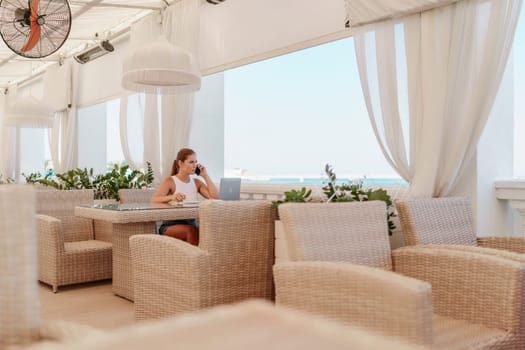 Woman coffee cafe laptop sea. Female freelancer using laptop on coffee break in modern cafe with sea view in the morning.