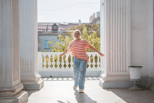A woman in a striped shirt is walking on a balcony. The balcony is surrounded by pillars and has a view of the city. The woman is enjoying the view and the fresh air