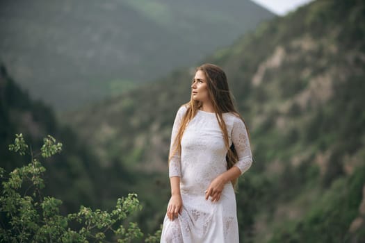 A woman in a white dress is standing on a mountain top. She is looking out over the landscape, taking in the beauty of the surroundings. Concept of peace and serenity