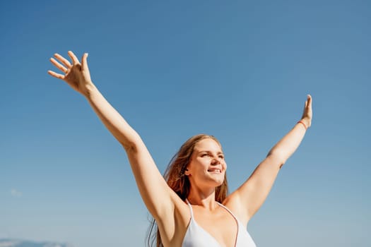 A woman is standing in the sun with her arms raised, smiling. Concept of joy and happiness, as the woman is enjoying the beautiful day