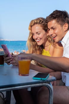 smiling woman and man enjoying vacation in a restaurant. Beautiful and cheerful Generation Z girls browsing the internet with smartphones.Vertical