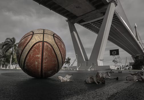 Basketball ball on the Old cement court floor at Outdoor park with Suspension bridge and Sky in the background. Space for text, Selective focus.