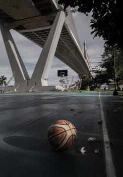 Basketball ball on the Old cement court floor at Outdoor park with Suspension bridge and Sky in the background. Space for text, Selective focus.